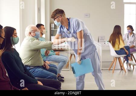 Man doctor in medical protective face mask bumping elbows with mature senior man patient before vaccination Stock Photo