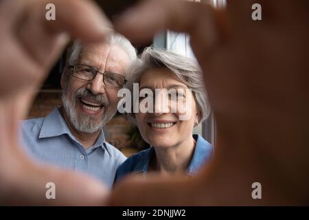 Happy bonding older family couple making heart sign with fingers. Stock Photo