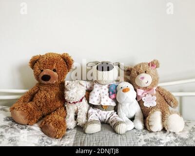 A row of children cuddly toy teddy bears in a cozy bedroom sitting together on a comfy bed with copy space Stock Photo