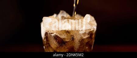 Close up banner of sparkling carbonated cold fresh cola drink being poured into the glass with overflowed frothy bubble on top Stock Photo