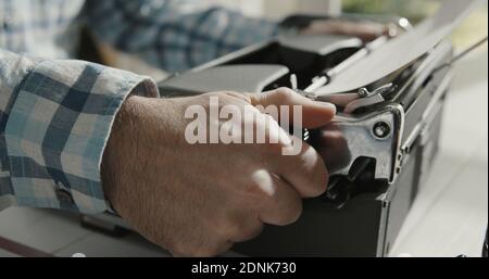 Man sitting at desk at home and typing on a vintage typewriter, creativity and storytelling concept Stock Photo