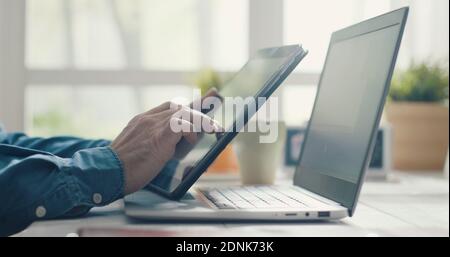 Man sitting at desk and working from home, he is using a digital tablet and a laptop Stock Photo