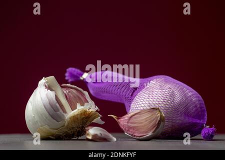Close up of a garlic lot in purple net and parts aside in studio with dramatic light and dark red background Stock Photo
