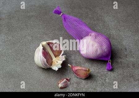 Metallic surface background with a garlic lot in purple net and parts aside in studio Stock Photo