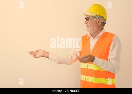 Profile view of handsome senior bearded man construction worker showing something while wearing eyeglasses against white background Stock Photo