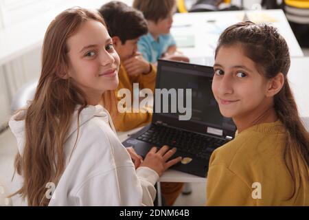 Happy teenage girls smiling to the camera while working on a school project together, using laptop Stock Photo