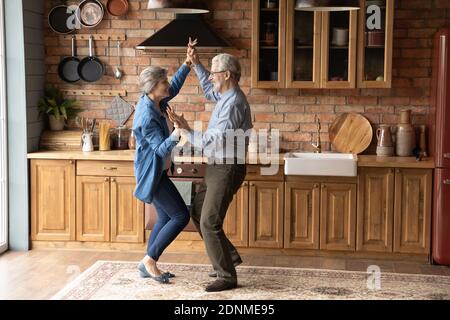 Energetic middle aged family couple dancing in kitchen. Stock Photo