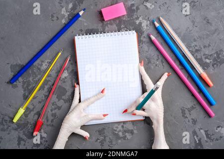 Painted chicken paw holds a pencil over a sheet of white paper for writing Stock Photo
