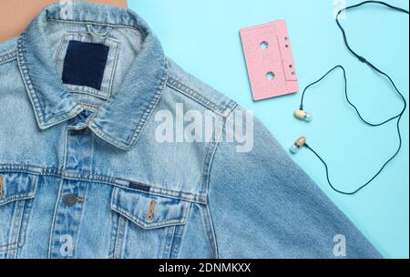 Jeans jacket, audio cassette, vacuum earphones on blue pastel background. Retro media, music lover, 80s. Top view, flat lay Stock Photo