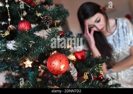 Munich, Deutschland. 17th Dec, 2020. Topic picture lonely Weihafterten 2020 in the coronavirus pandemic. A young woman with face mask, mask sits alone behind her Weihaftertsbaum on Christmas Eve and is sad. MODEL RELEASED! | usage worldwide Credit: dpa/Alamy Live News Stock Photo