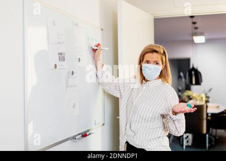 Woman wearing protective face mask writing on whiteboard Stock Photo