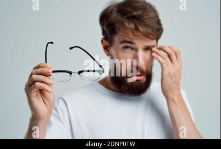 a man with narrowed eyes holds glasses in his hand on a light background vision problems Stock Photo