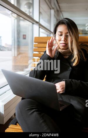 Woman at train station using laptop Stock Photo