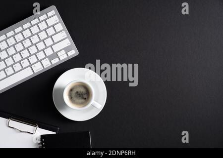 Black office desk table with computer keyboard, cup of coffee, clipboard, notepad. Luxury, minimalist style workspace. Flat lay, top view, copy space. Stock Photo