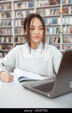 Vertical portrait of a young Asian female student working on her laptop at local library Stock Photo