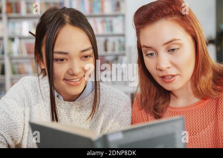 Cropped shot of two young female friends reading a book together at college library. Female students reading Stock Photo