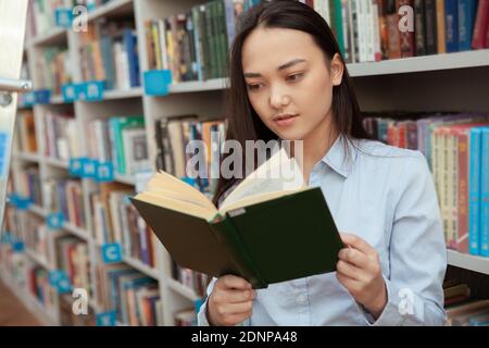 Young Asian woman reading a book at the library. Attractive female student shopping for books at bookstore Stock Photo