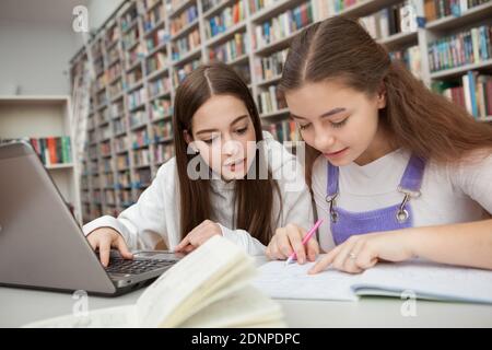 Two teen schoolgirls working on a project together at the library. Studying, learning concept Stock Photo