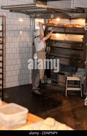 Female baker taking bread out of oven Stock Photo