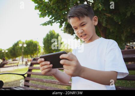 Low angle shot of a young Asian boy looking angry, playing online games on his smart phone. Little boy losing in online games, making furious face Stock Photo