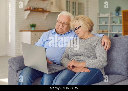 Happy senior couple sitting on couch with laptop, video calling family or shopping online Stock Photo