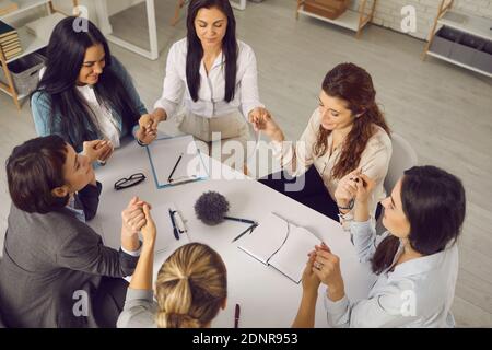 Group of supportive business women sitting around office table and holding hands Stock Photo