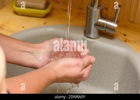 In the palm of the girl pouring water from the tap in the sink Stock Photo
