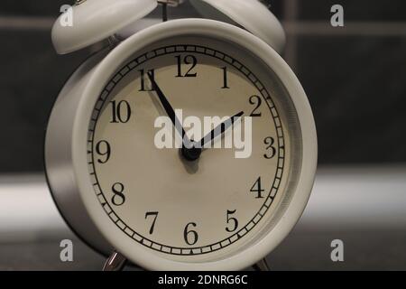 Round clock-alarm white on a gray background, isolated, close-up. Stock Photo