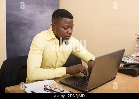 young confident and smiling businessman sitting alone at a desk and working on a laptop Stock Photo