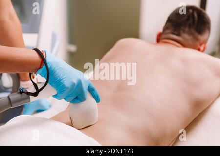 Unrecognizable man getting laser hair removal on his lower back, copy space. Beautician removing lower back hair of a male client, using laser Stock Photo