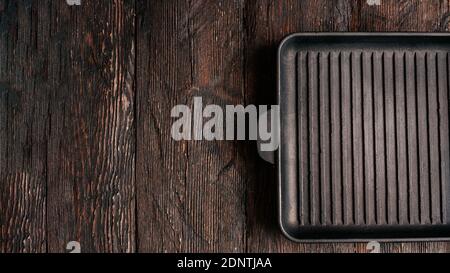 New empty cast-iron grill pan with two handles on wooden background. place for text. Flat lay top view black cast iron skillet for barbecue. Food Mock Stock Photo