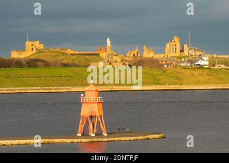 The Herd Groyne lighthouse and Tynemouth castle and priory buildings seen from South Shields, north east England, UK Stock Photo