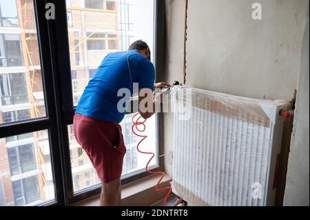 Back view of plumber filling pipes with pressurized air to inspect for leaks in new installation, using air compressor while checking gas tightness of heating system. Concept of gas tightness testing. Stock Photo