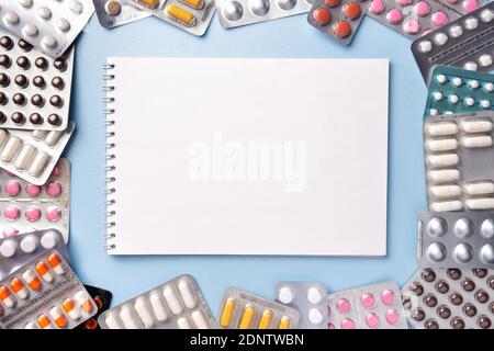 Bunch of pills of different colors in blisters pack on blue background with notebook, copy space. Prescription blank for medicine drug recipe. Pharmac Stock Photo