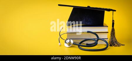 medical education - college graduation cap with stethoscope and books on yellow background with copy space Stock Photo