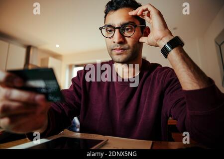 Stressed mixed race business man attempting to make online payments while holding credit card  Stock Photo