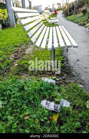 Stainless steel lated bench seating with empty beer cans left on the floor. Stock Photo