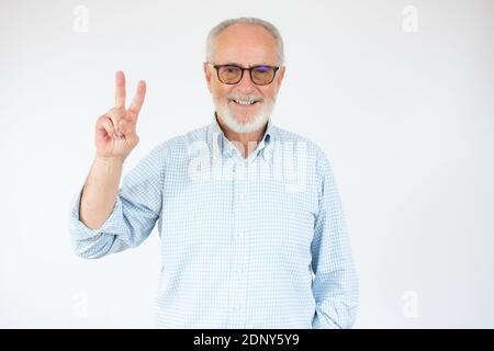Senior grey-haired man wearing casual shirt standing over isolated white background smiling with happy face looking at the camera doing victory sign w Stock Photo