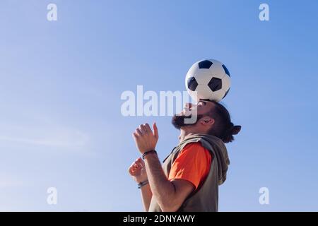 portrait of a football player playing balancing the ball on his head with a clear blue sky in the background, concept of healthy lifestyle and urban s Stock Photo