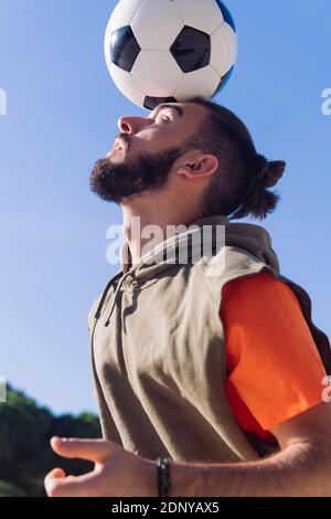 vertical portrait of a football player playing balancing the ball on his head with a clear blue sky in the background, concept of healthy lifestyle an Stock Photo