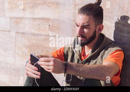 attractive sportsman with earphones to listen to music checking his smart phone, concept of technology and urban sport lifestyle in the city, copy spa Stock Photo