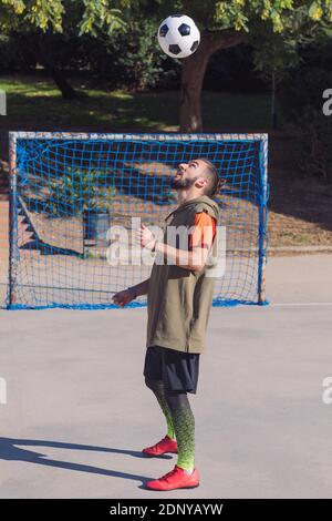 vertical photo of a soccer player playing giving head hits to the the ball in a concrete soccer field, concept of healthy lifestyle and urban sport in Stock Photo