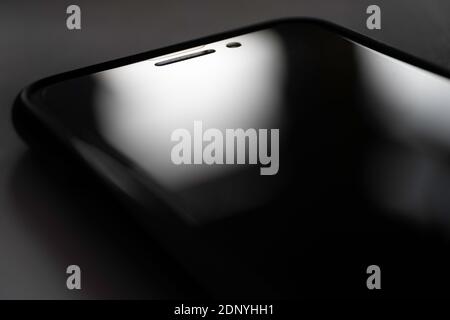 Gaze at the shiny black screen of a black smartphone lying on a dark table Stock Photo