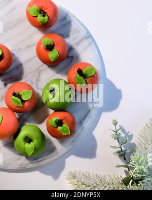 Marzipan sponge apples, green and red. Panoramic flat lay on marble board with winter greens. Stock Photo