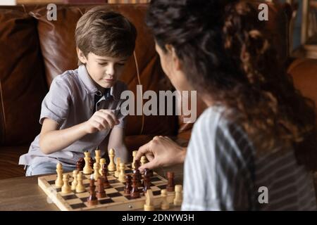 Smart little boy enjoying playing chess game with millennial mother Stock Photo