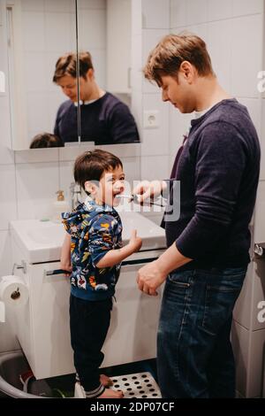 Father helping son brush his teeth Stock Photo