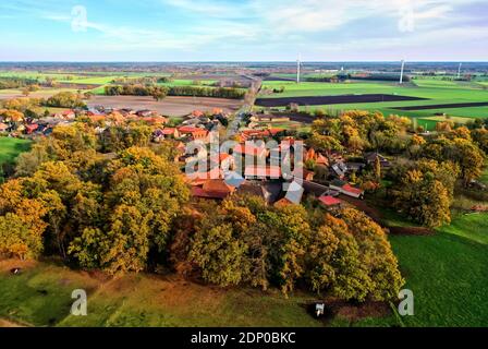 Aerial view of a small village in Germany with trees at the edge of the village and wind turbines on the horizon of the flat landscape Stock Photo