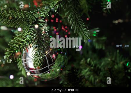shimmering silver christmas tee ornament hanging from a christmas tree surrounded by multi-colored bokeh lights Stock Photo