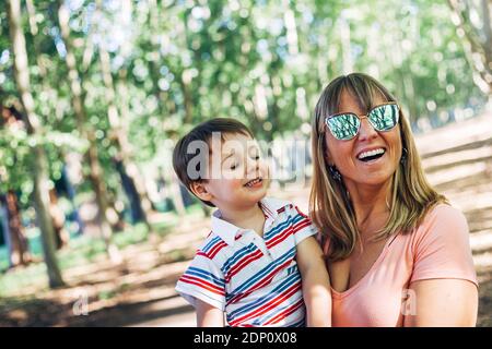 Happy mom laughing with her little son in her arms. Family day in the forest park. Mother's day concept. Caucasian small child smiling. Copy space. Stock Photo