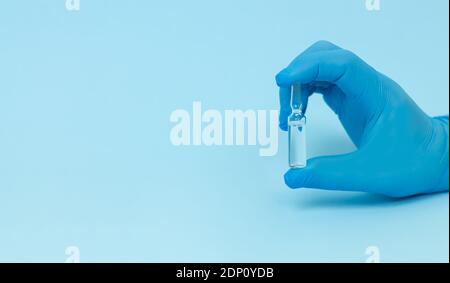 Doctor's hand in glove holding medical glass ampoule on blue background. Space for text Stock Photo